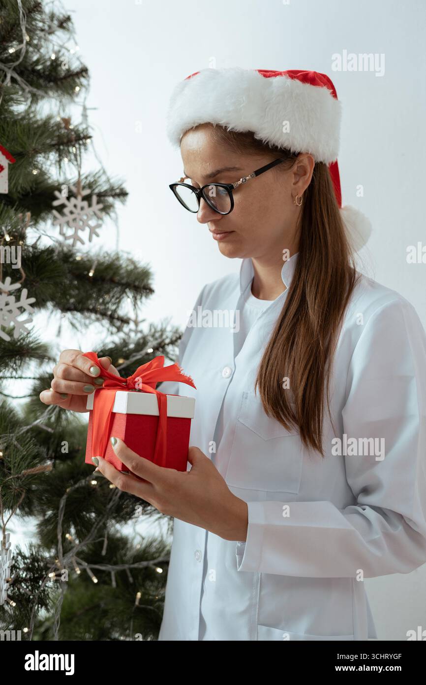 Portrait de femme médecin en manteau blanc et chapeau de père noël tenant la boîte cadeau de Noël sur le quart de travail la veille de noël à l'hôpital. Vacances, médecine et voiture de santé Banque D'Images