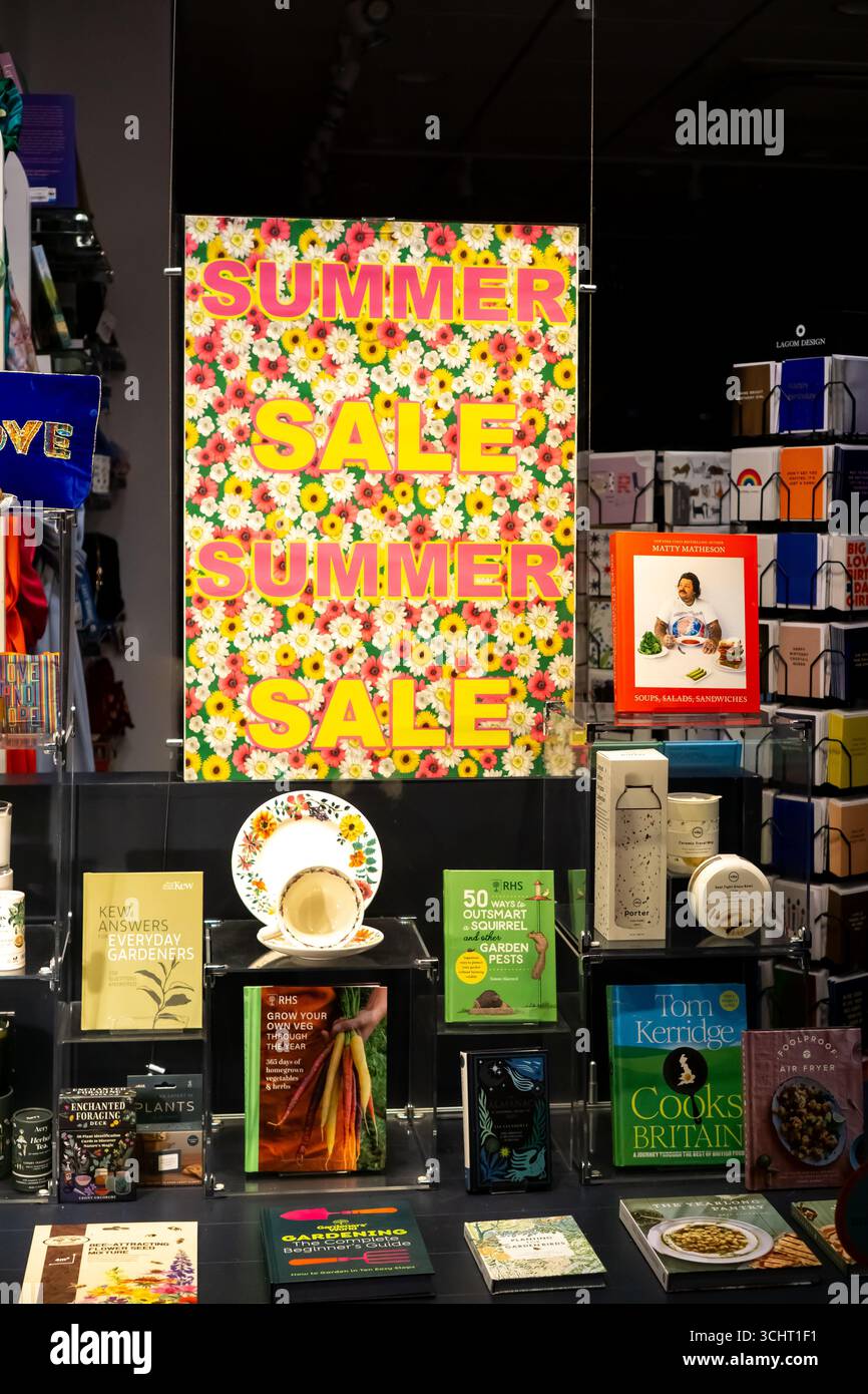Une vitrine de librairie la nuit annonce une vente estivale. Les livres et autres articles sont sur les étagères ci-dessous. Banque D'Images