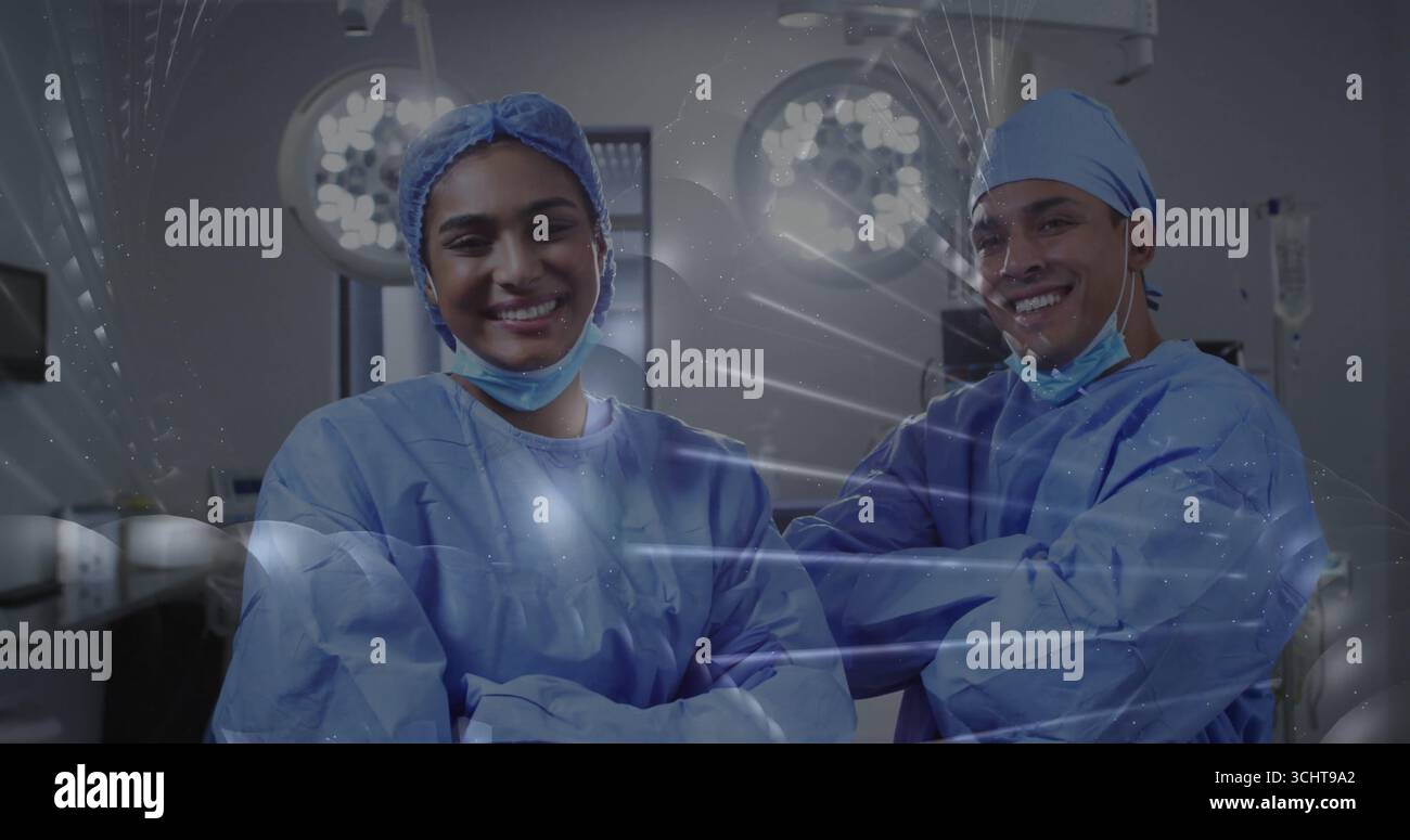 Sourire deux chirurgiens vêtus de blouses bleues posant dans la salle d'opération, avec des plafonniers et des moniteurs Banque D'Images