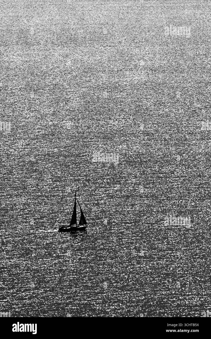 Voilier silhouette sur la surface de l'eau chatoyante en noir et blanc, Tihany, Lac Balaton, Hongrie, en format vertical Banque D'Images