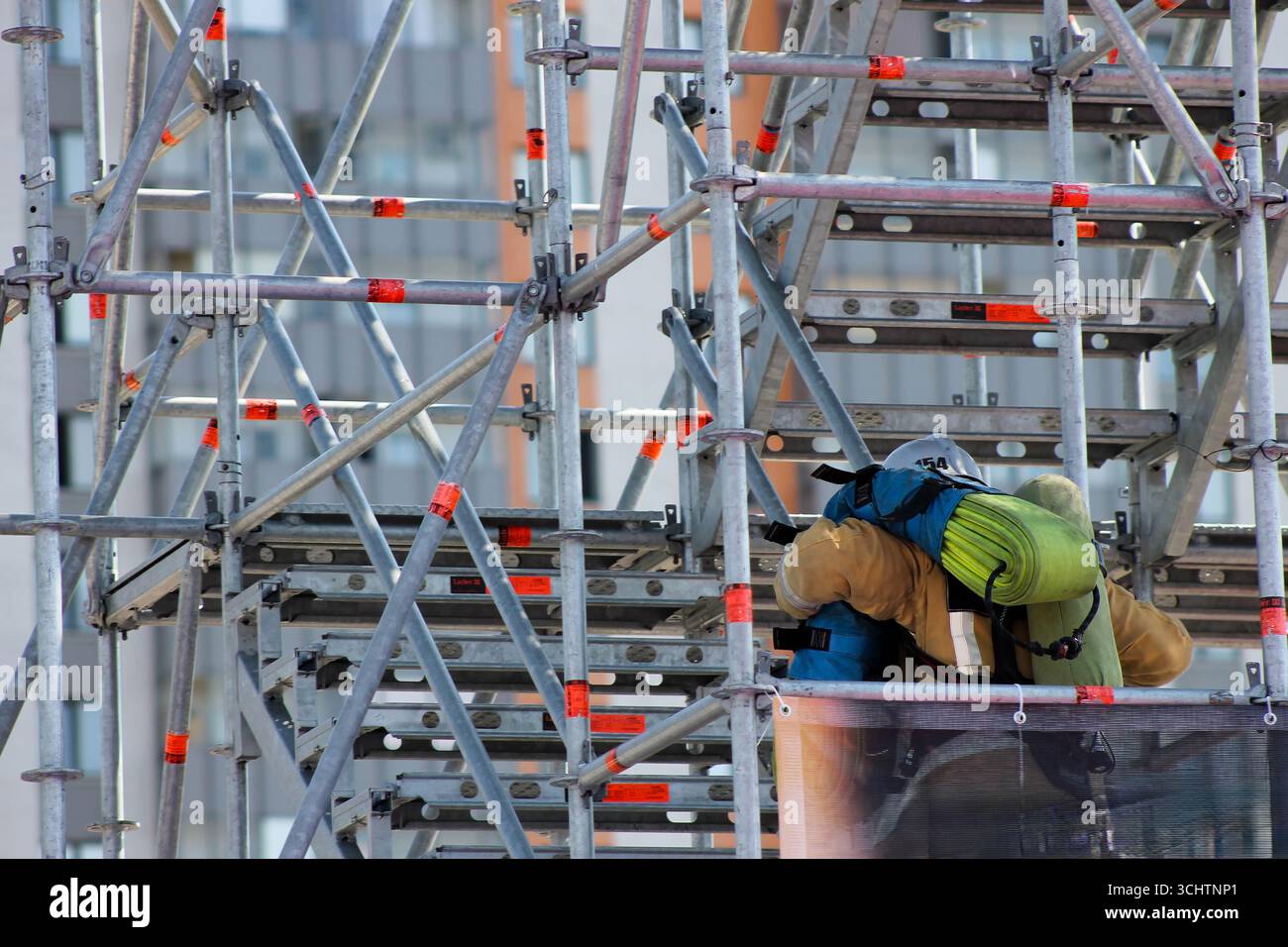 Un homme travaille sur une structure d'échafaudage. Il porte une veste jaune et un sac à dos Banque D'Images