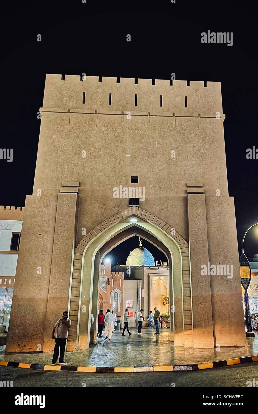 Les visiteurs traversent une passerelle historique sous un éclairage nocturne spectaculaire, à Muscat City/19 juillet 2025, Muscat, Oman. Banque D'Images