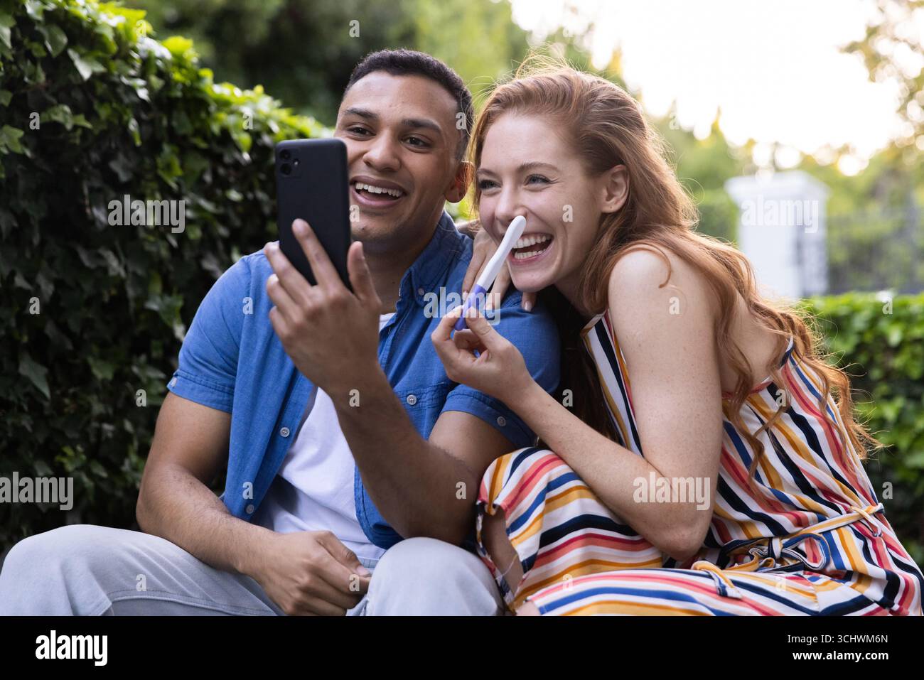 Célébrant le résultat positif du test de grossesse, joyeux appel vidéo de couple diversifié dans le jardin Banque D'Images