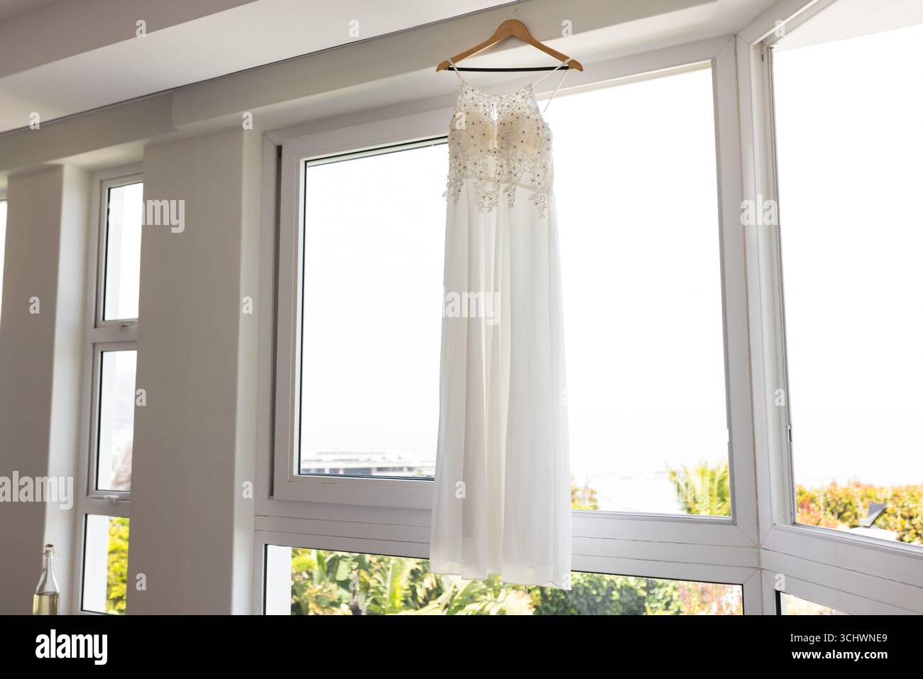 Élégante robe de mariée blanche suspendue par une grande fenêtre dans une pièce lumineuse Banque D'Images