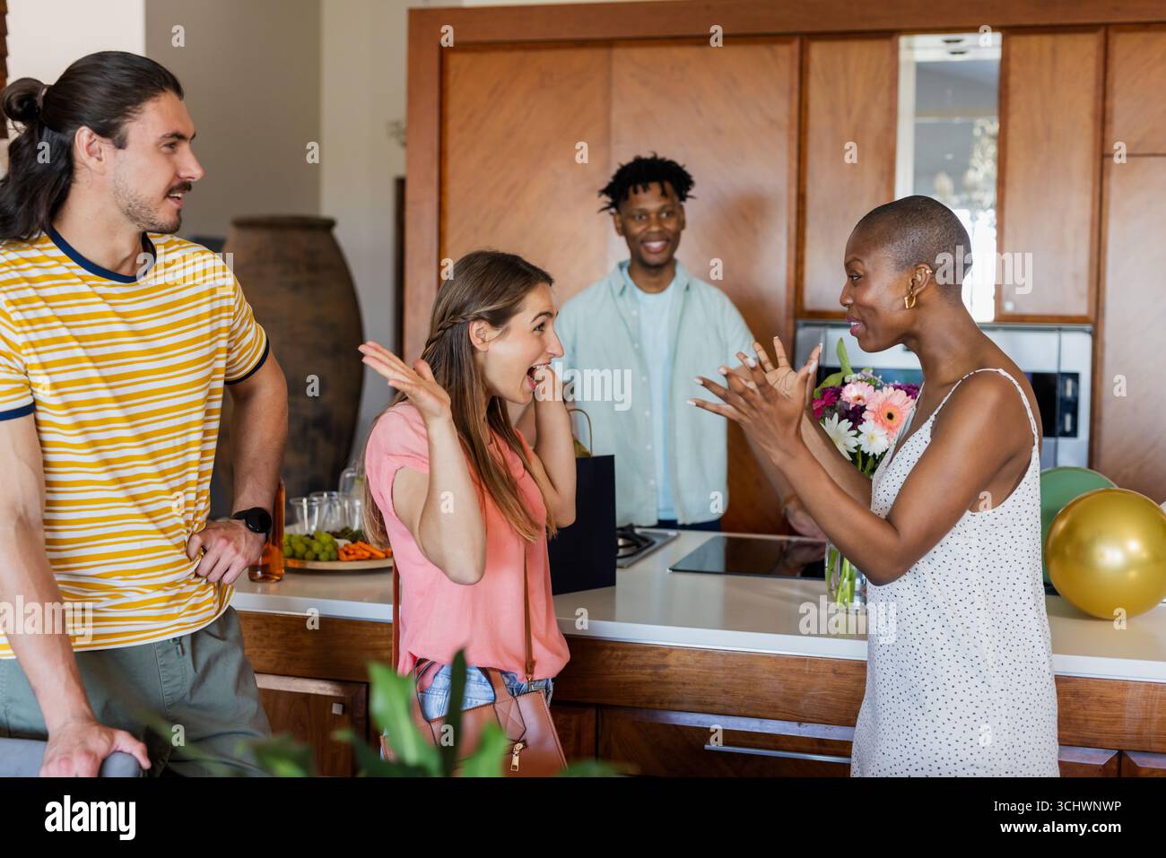 Célébrer à la maison, amis souriant et discutant autour du comptoir de cuisine avec des ballons Banque D'Images