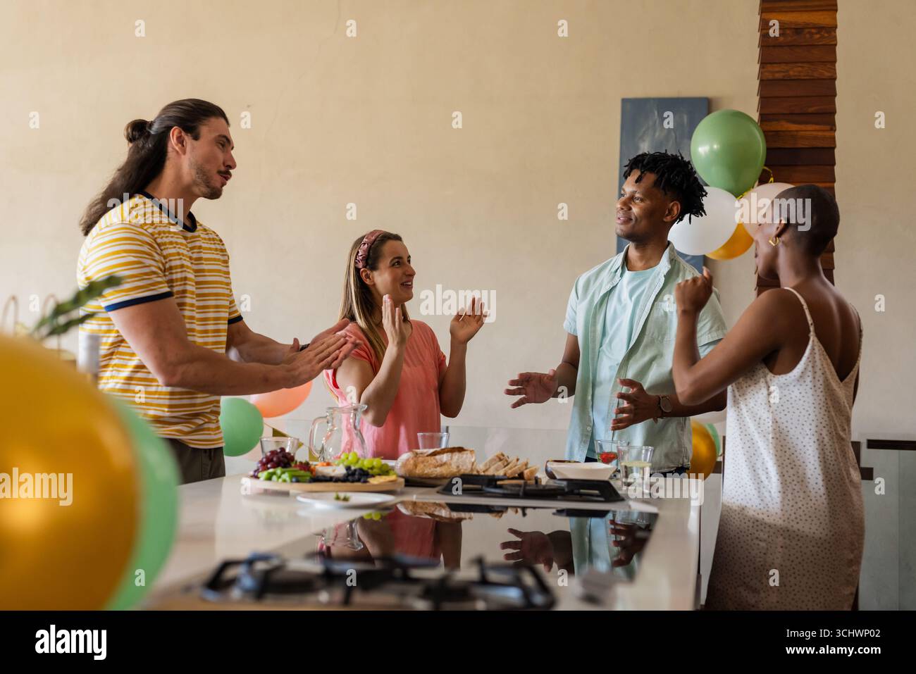 Célébrant à la maison, des amis partageant la conversation et riant autour de l'îlot de cuisine Banque D'Images