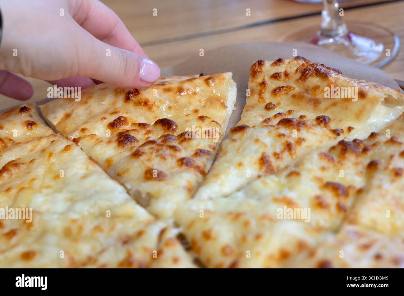 Un délicieux pain plat à l'ail au fromage, fraîchement cuit et tranché, avec une main tendue pour un morceau. Parfait pour partager lors de rassemblements ou profiter en tant que sn Banque D'Images