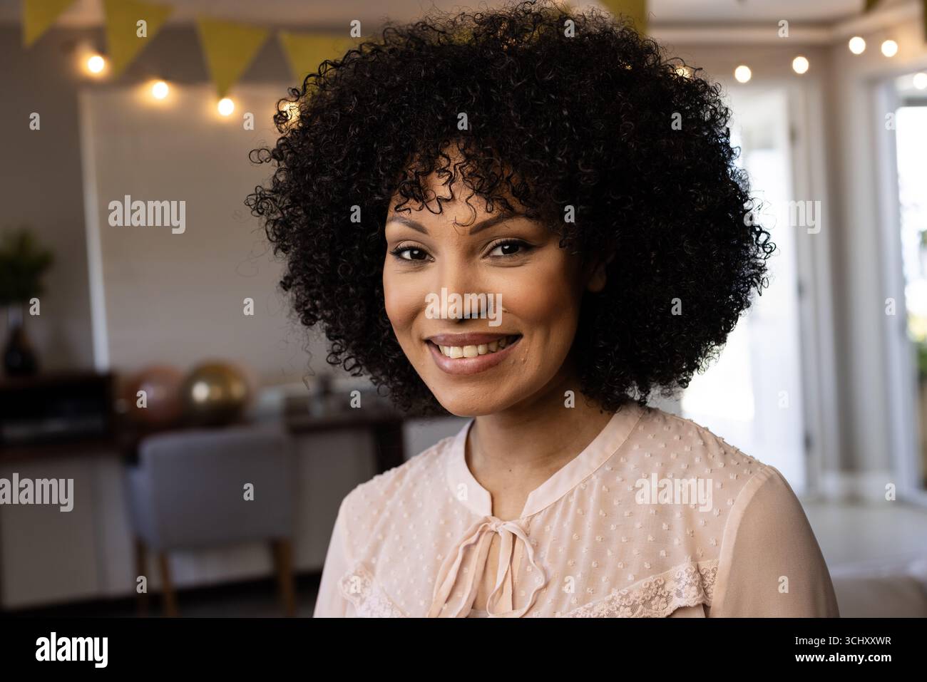 Femme souriante avec les cheveux bouclés appréciant la célébration festive à la maison Banque D'Images