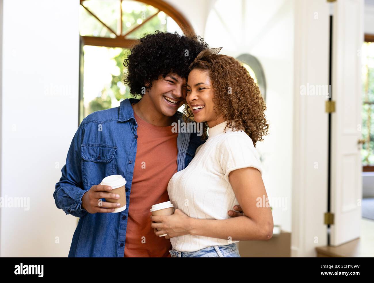 Jeune couple diversifié appréciant le café ensemble à la maison, partageant le rire et le bonheur Banque D'Images