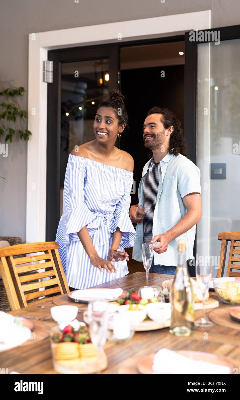 Jeune couple multiracial profitant sur le patio brunch, souriant et bavardant à la table en bois Banque D'Images