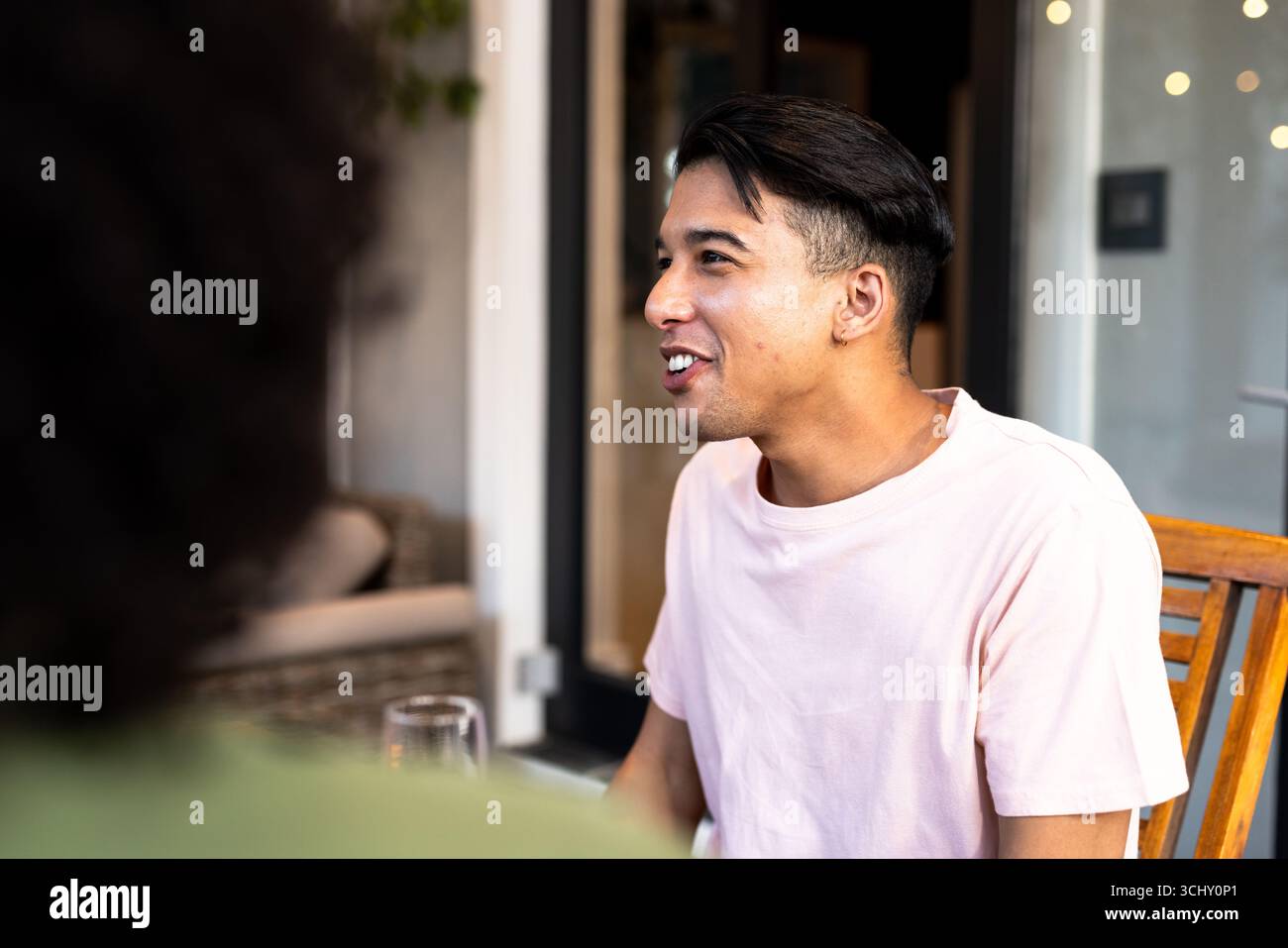 Jeune homme souriant et parlant avec des amis multiraciaux au café sur patio Banque D'Images