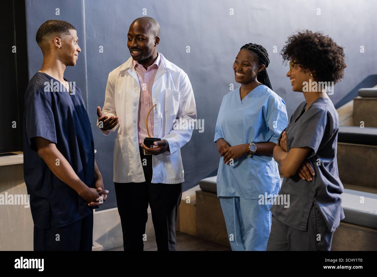 Docteur titulaire d'un prix, souriant avec des professionnels de la santé dans les gommages discutant à l'hôpital Banque D'Images