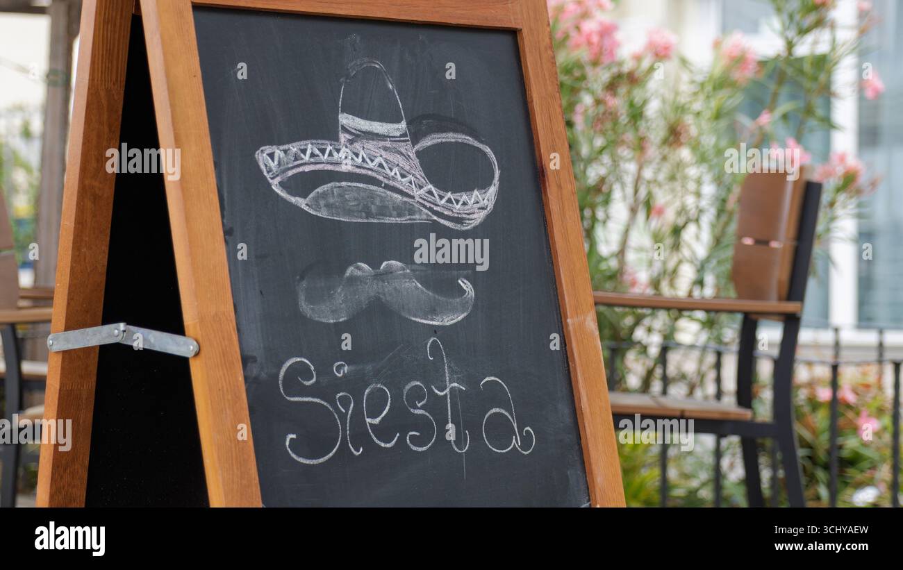 Un panneau en bois indique les heures de sieste de 14 à 18 dans un restaurant, entouré de tables vides et de décor floral. Banque D'Images