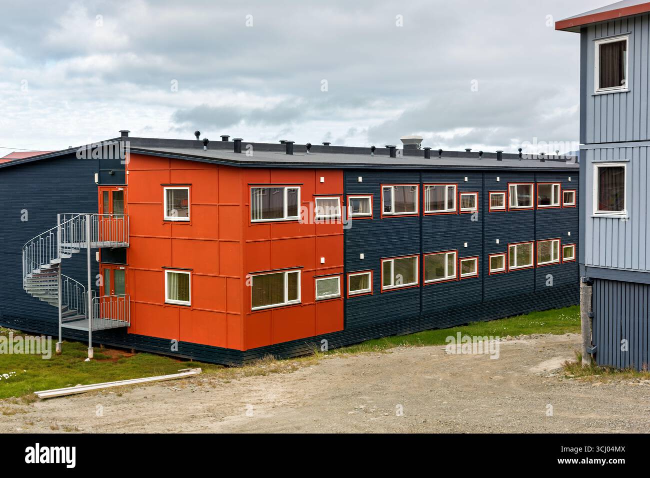 Bâtiments modernes avec escalier en colimaçon Longyearbyen Svalbard Norvège // LONGYEARBYEN, SVALBARD — des bâtiments modernes avec un escalier en colimaçon proéminent sont visibles à Longyearbyen, Svalbard et Jan Mayen. Les structures présentent des couleurs contrastées, avec une section peinte en orange vif et le corps principal en bleu foncé. L'architecture reflète les besoins fonctionnels de la colonie arctique, qui est le centre administratif et le plus grand établissement du Svalbard. Longyearbyen est connue pour son environnement unique et son rôle de porte d'entrée vers la nature sauvage de l'Arctique. Banque D'Images