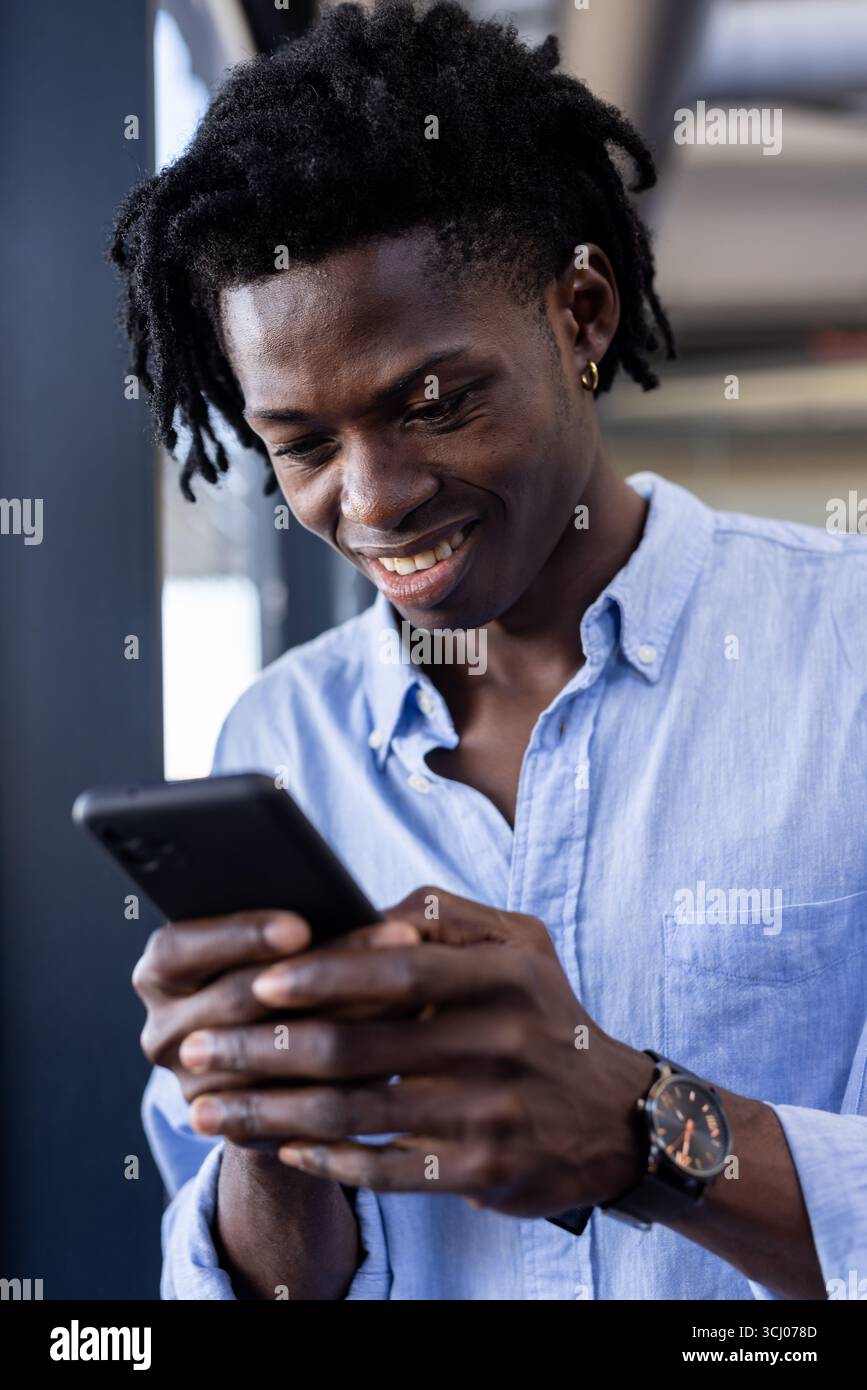 Homme souriant à l'aide d'un smartphone au bureau, s'engager avec du contenu numérique Banque D'Images