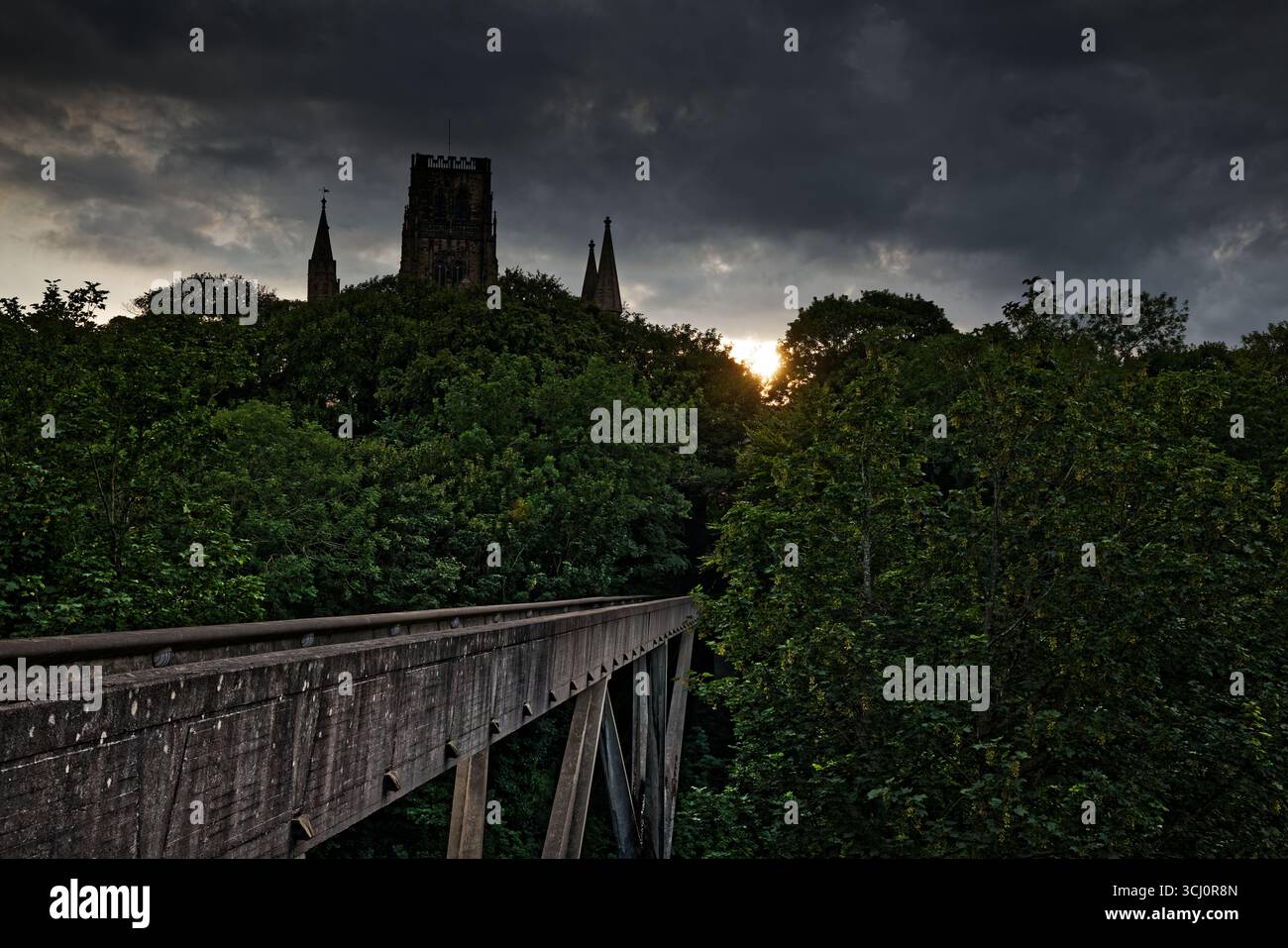 Les anciennes tours et pinacles s'élèvent au-dessus d'une canopée d'arbres au coucher du soleil avec une passerelle traversant la rivière Wear, Durham, Angleterre. Banque D'Images