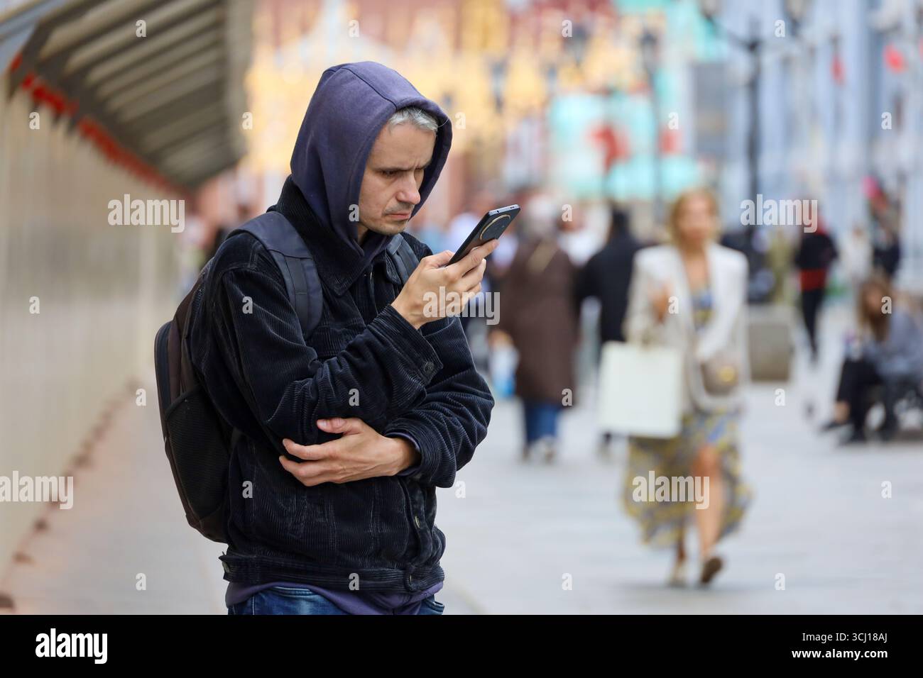 Homme à l'aide d'un smartphone sur la rue de la ville à l'automne debout sur fond de personnes floues Banque D'Images