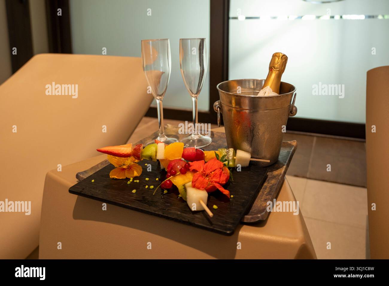 Un plateau de fruits et de champagne est posé sur une table. Le champagne est dans un seau argenté et le fruit est sur une assiette noire. La scène est festive et festi Banque D'Images