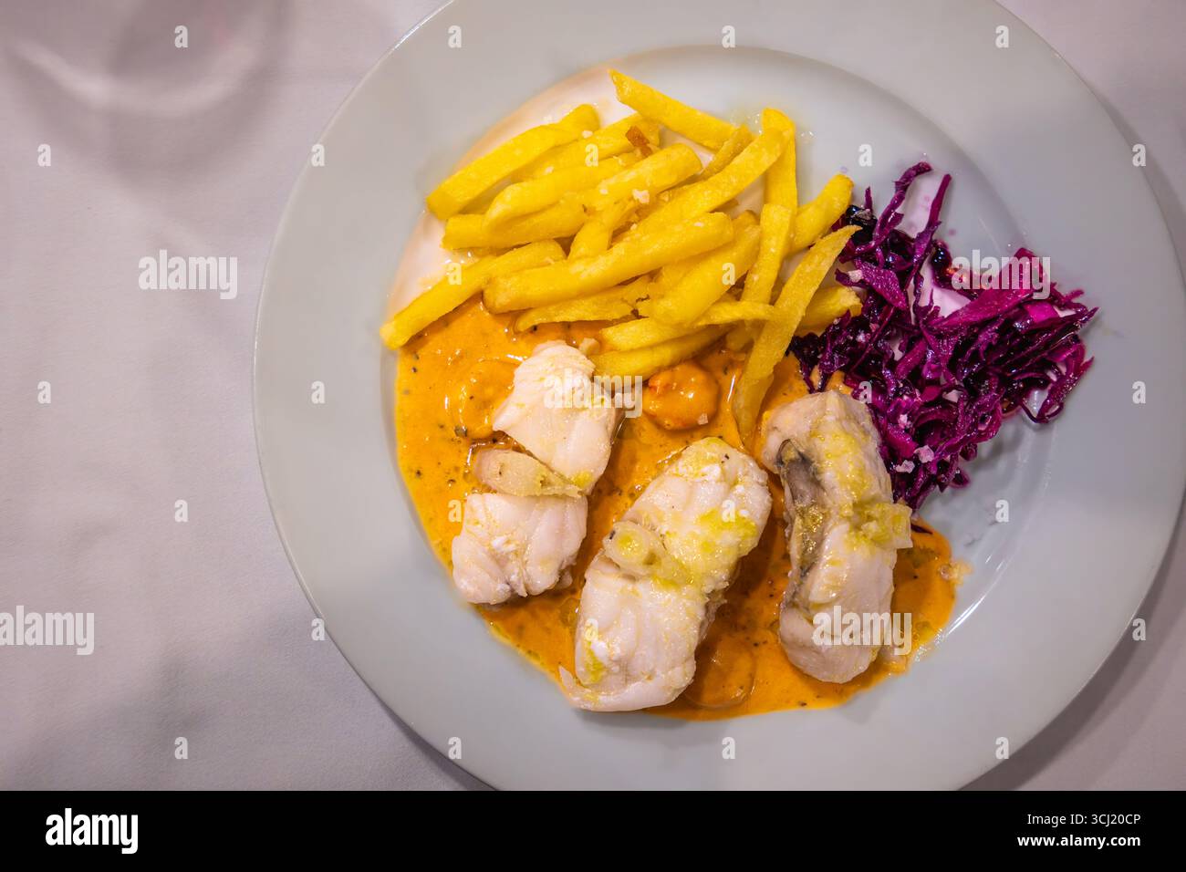 Antequera, Espagne - 12 mars 2025 : plat de filets de poisson blanc avec sauce orange, frites et chou. Servi dans un restaurant rustique dans un oliv Banque D'Images
