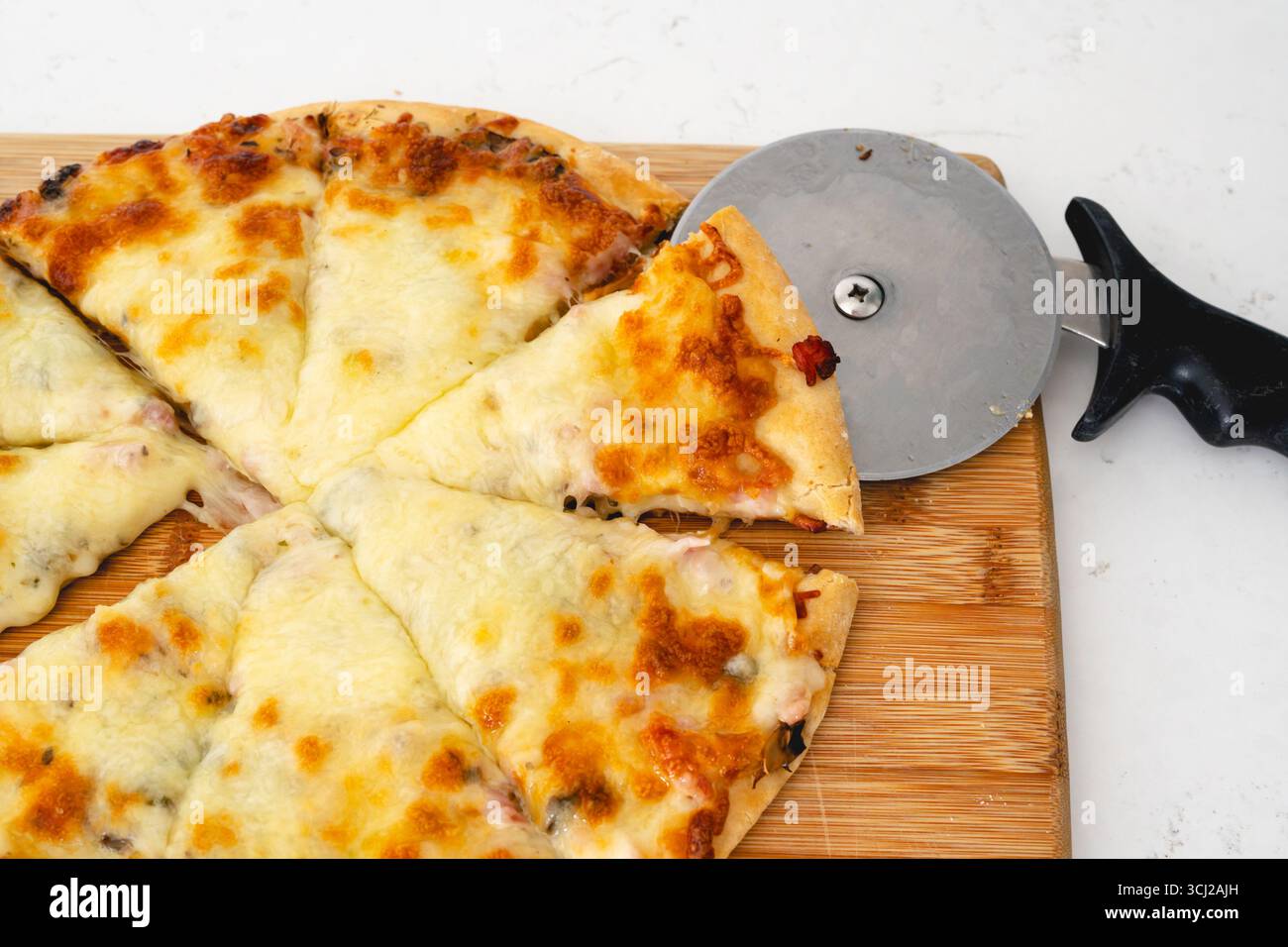 Une vue rapprochée montre un coupe-pizza tranchant une pizza au fromage sur une planche de bois. Banque D'Images