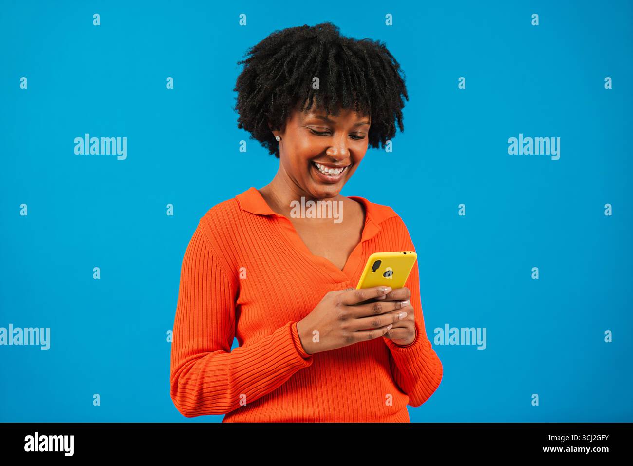 Femme joyeuse s'engageant joyeusement avec son smartphone, absorbée par du contenu divertissant sur son appareil mobile, incarnant la joie du numérique Banque D'Images
