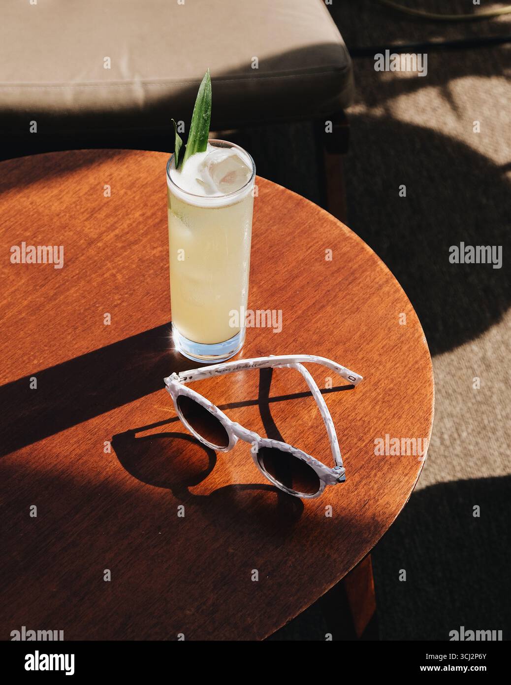 scène de vacances d'été classique avec un grand cocktail tropical rafraîchissant et une élégante paire de lunettes de soleil reposant sur une table en bois ensoleillée. Banque D'Images