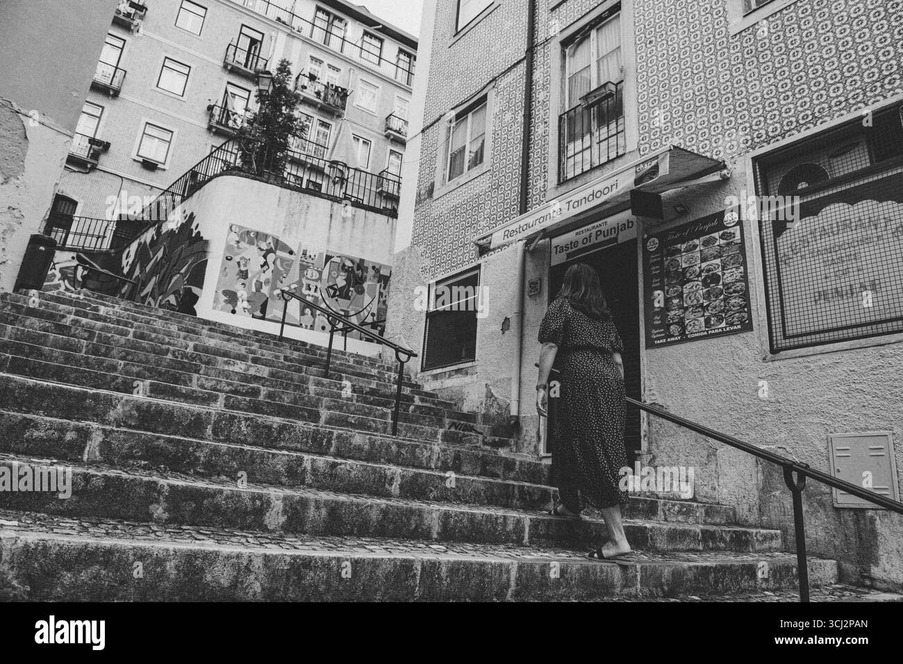 Photo en noir et blanc à angle bas d'une personne montant un escalier pavé à Lisbonne. La scène présente une architecture portugaise classique, includi Banque D'Images