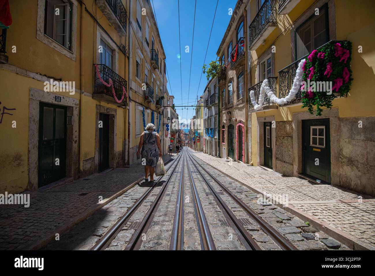 Une photo grand-angle et basse d'une rue escarpée de Lisbonne, mettant en valeur les voies de tramway emblématiques, les pavés classiques et un mélange d'architecture historique Banque D'Images