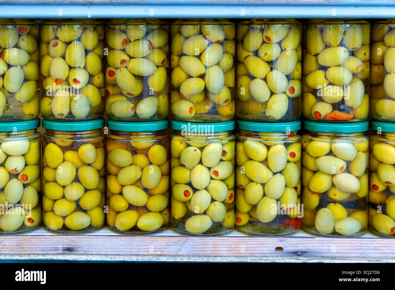 Bocaux d'olives vertes marinées sur l'affichage. Bocaux en verre remplis d'olives vertes conservées dans la saumure, soigneusement empilés avec des couvercles verts, créant un coloré Banque D'Images