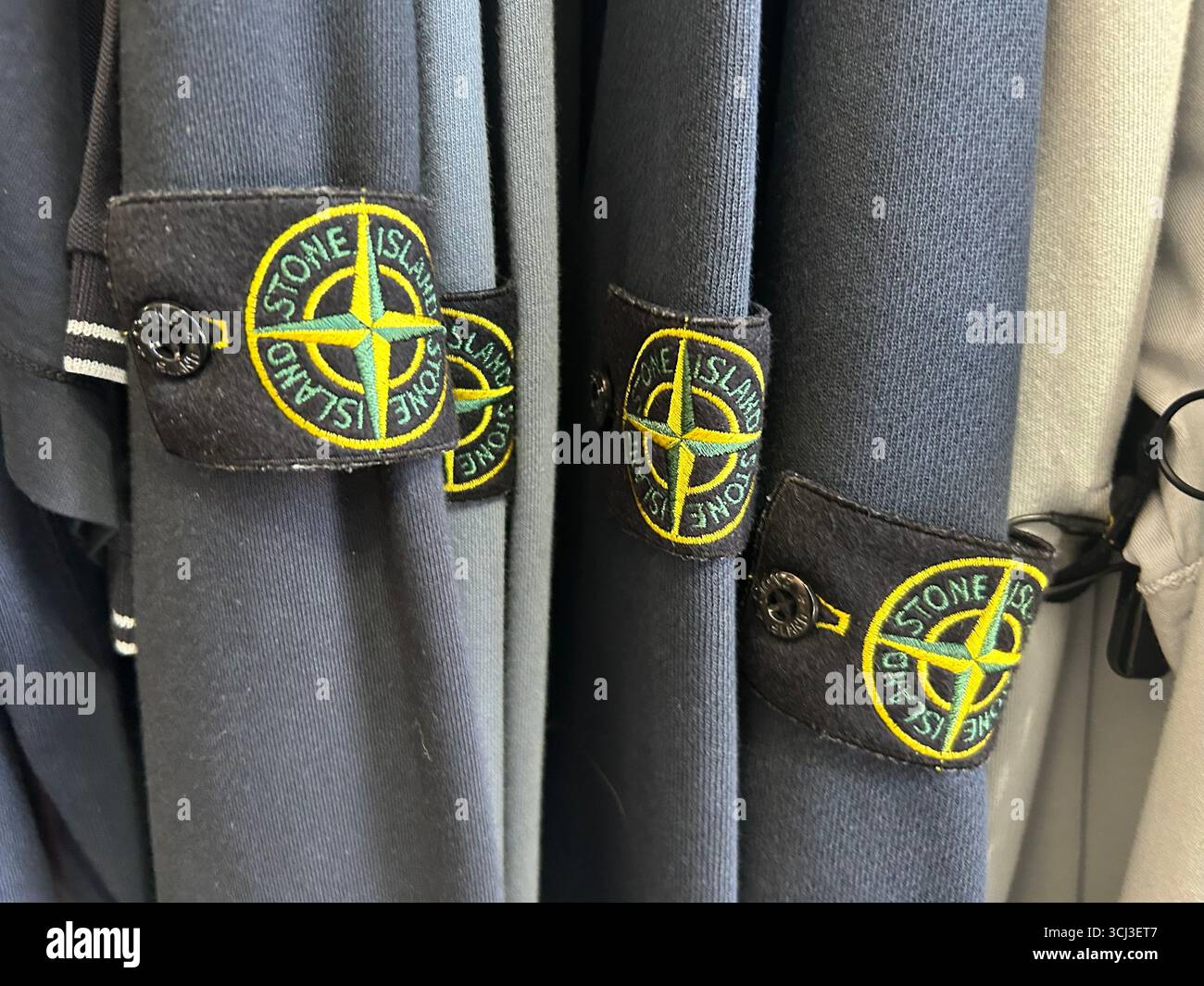 Badges Stone Island montrés sur les manches des vêtements, souvent associés à des vêtements de hooliganisme de football, en vente dans un magasin de vêtements de Londres, Royaume-Uni - Image de stock capturée avec un smartphone