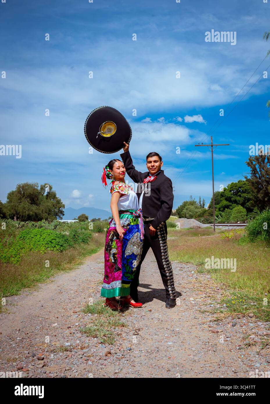 Jeune couple mexicain portant des costumes folkloriques, avec l'homme dans un costume noir charro mariachi et la femme dans une jupe brodée vibrante, Celebratin Banque D'Images