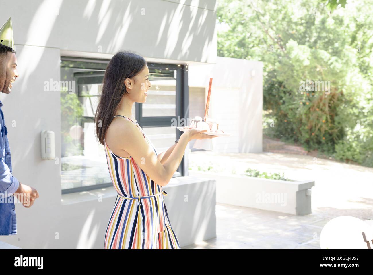 Portant gâteau avec bougie, femme en robe rayée célébrant à l'extérieur Banque D'Images