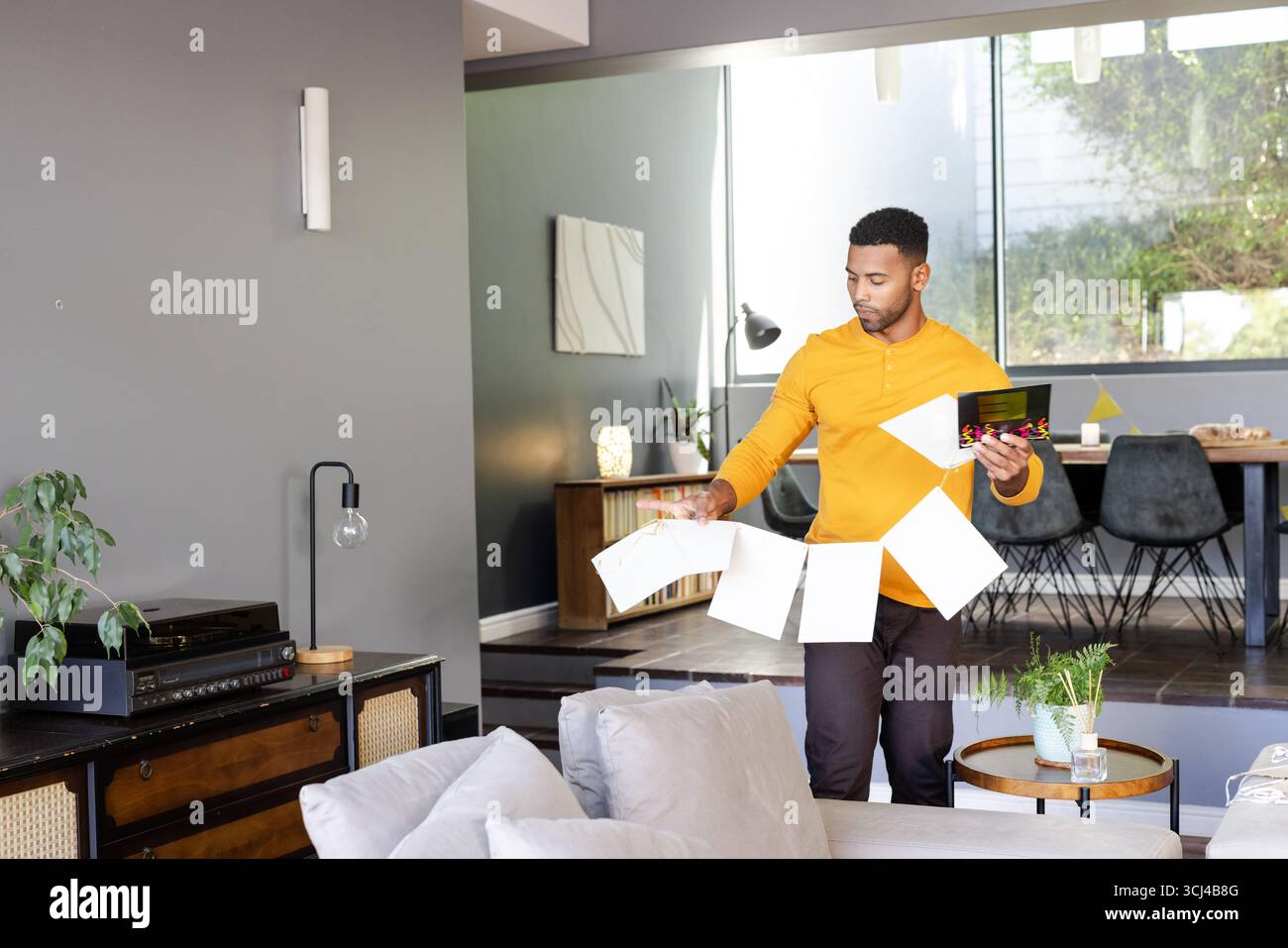 Homme dans le salon tenant des cartes de voeux, se préparant pour la célébration Banque D'Images