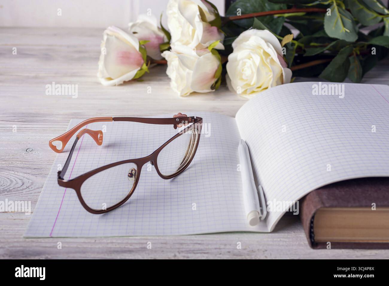 Un cahier ouvert, des verres, un bouquet de roses reposent sur la table Banque D'Images