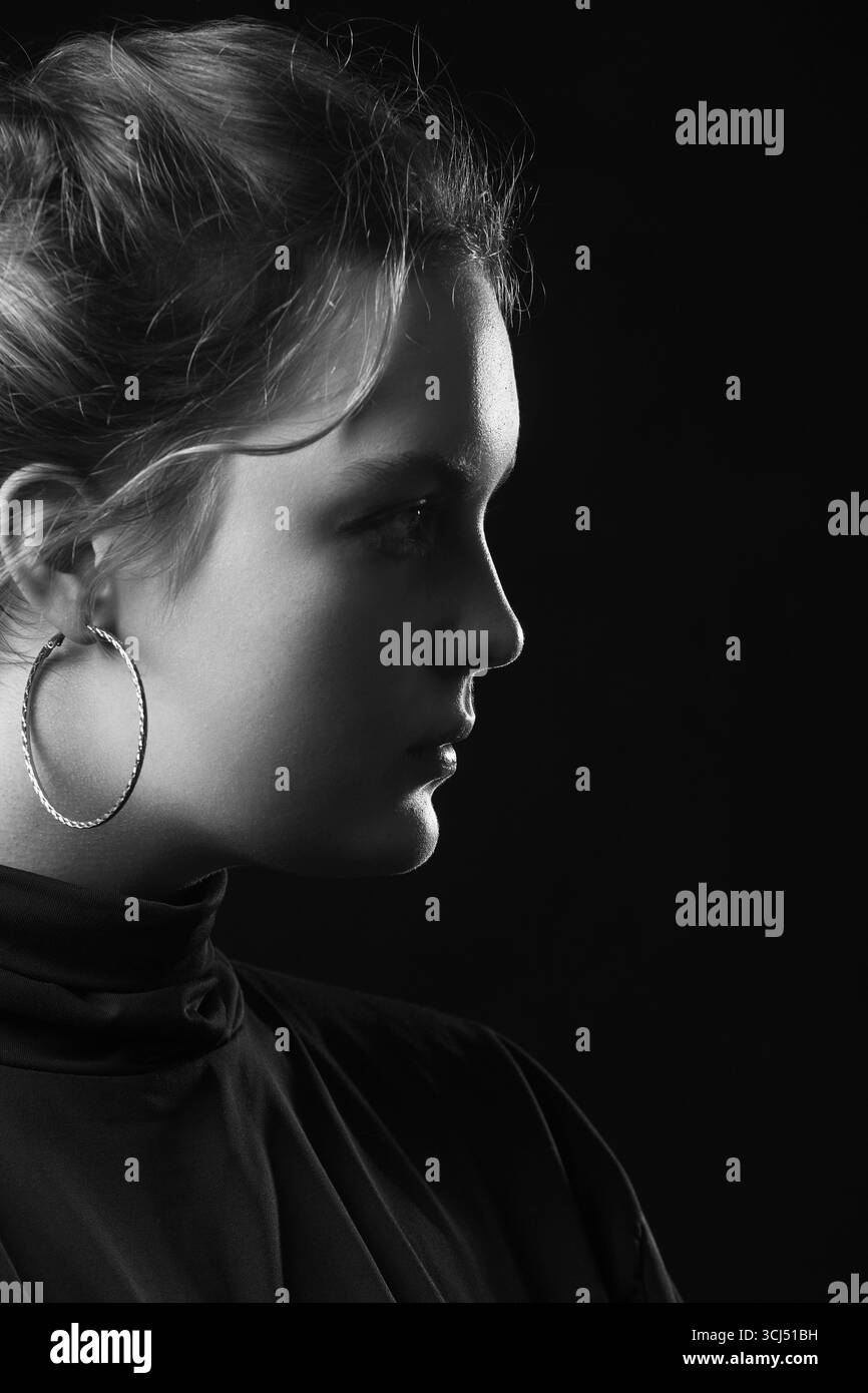 Jeune femme triste sérieuse avec syndrome de Down sur fond noir vue de profil latérale, monochrome Banque D'Images