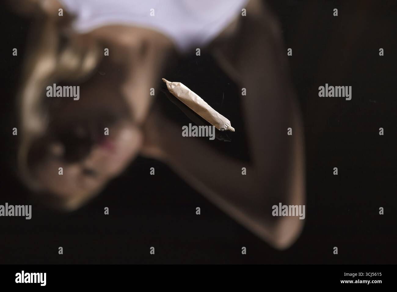 Joint avec de la marijuana sur fond de miroir noir avec réflexion floue féminine Banque D'Images