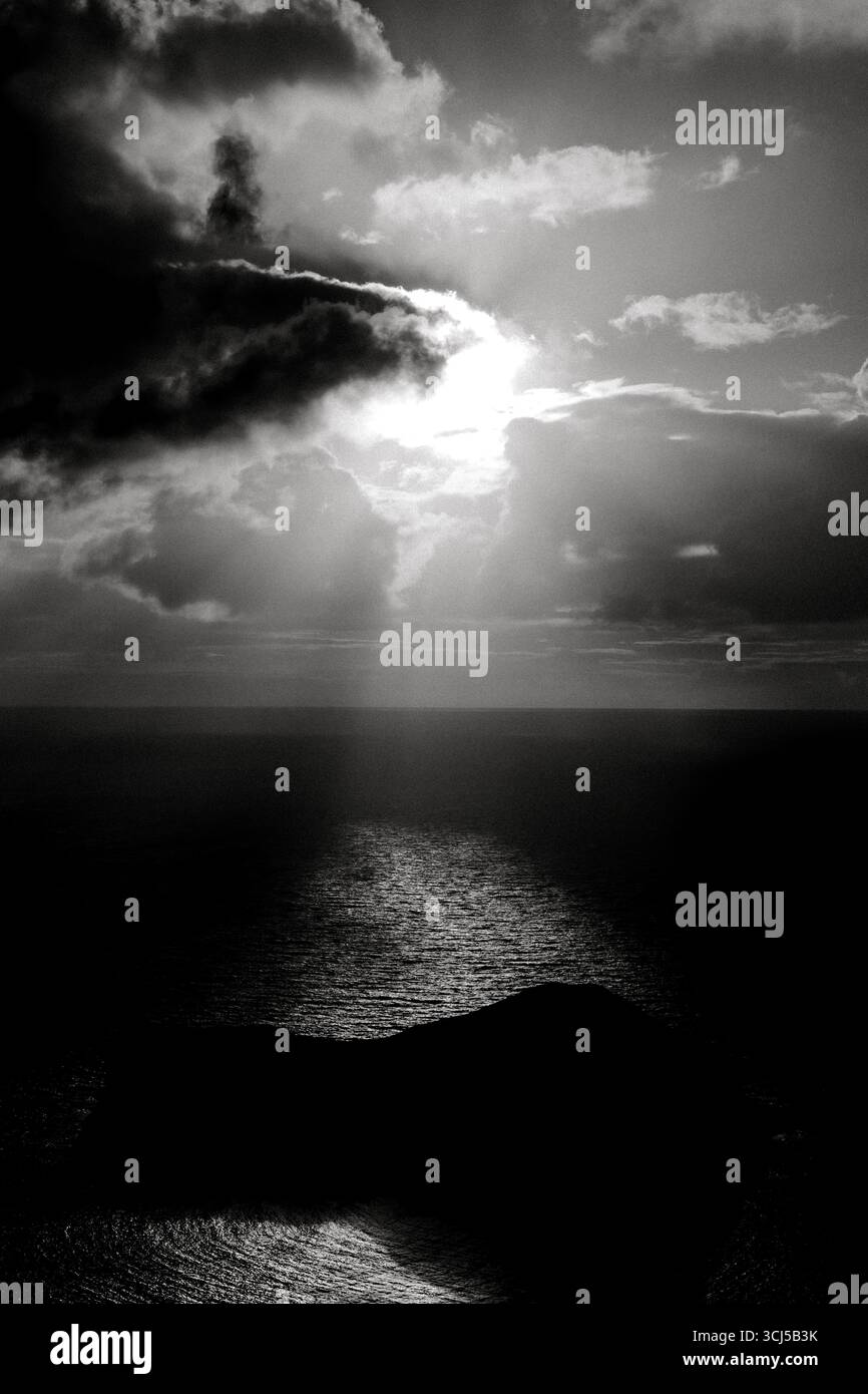 Noir un soleil blanc rayonnant à travers les nuages au-dessus de l'île rocheuse Banque D'Images Noir un soleil blanc rayonnant à travers les nuages au-dessus de l'île rocheuse Banque D'Images