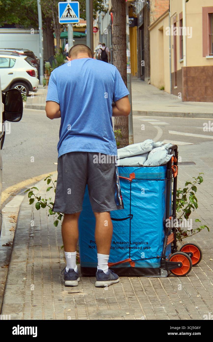 Viladecans. Barcelone - 05 septembre 2025 : un chauffeur Amazon Logistics, vu de derrière, organise les colis sur son chariot de livraison pliable avant cont Banque D'Images