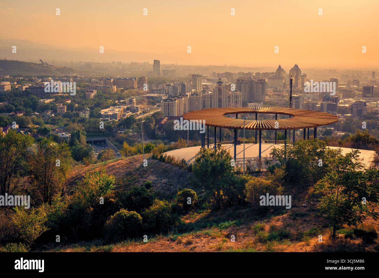 Vue panoramique du centre-ville d'Almaty, Kazakhstan, vu de la montagne Kok Tobe au coucher du soleil, avec un point de vue le long du sentier de randonnée visible au premier plan Banque D'Images