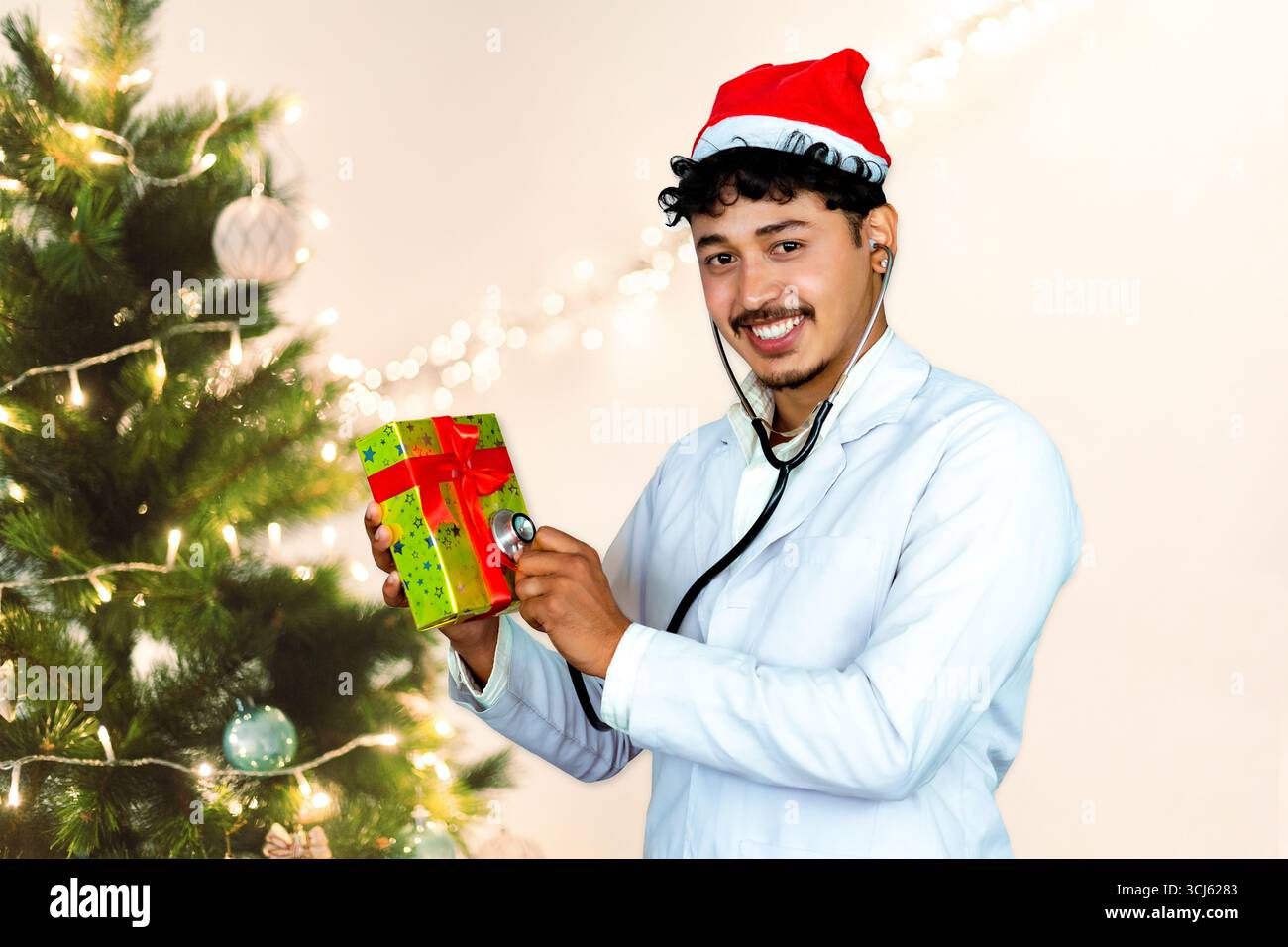Beau médecin masculin portant un chapeau de Père Noël, debout devant un arbre de Noël avec des cadeaux, célébrant la saison des fêtes dans un setti de soins de santé Banque D'Images