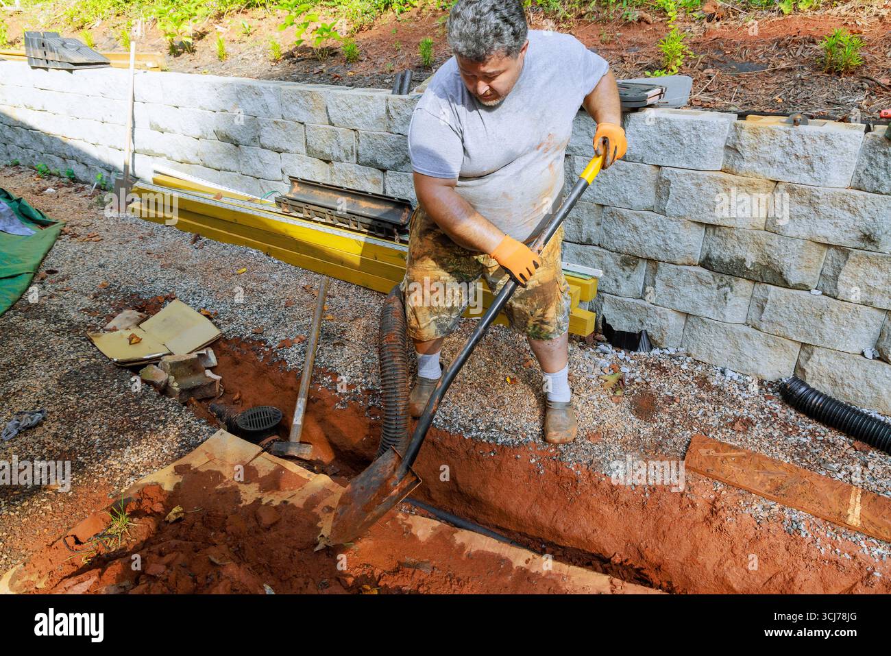 Le travailleur utilise une pelle pour creuser une tranchée dans le jardin pour un nouveau projet de système de drainage extérieur sur la journée de travail. Banque D'Images