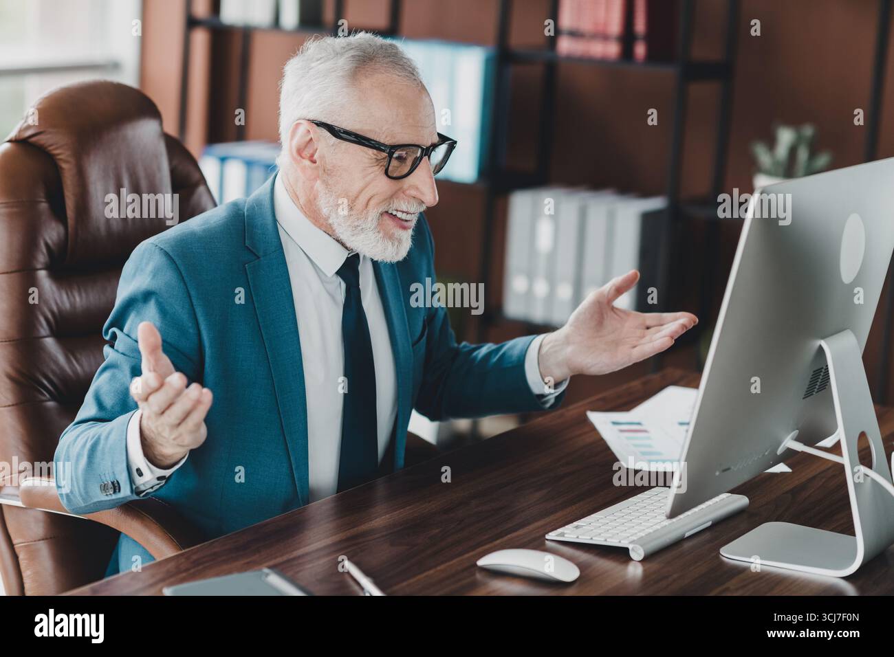 Homme d'affaires mature dans un costume formel s'engageant avec des collègues lors d'une réunion en ligne dans un environnement de bureau moderne Banque D'Images