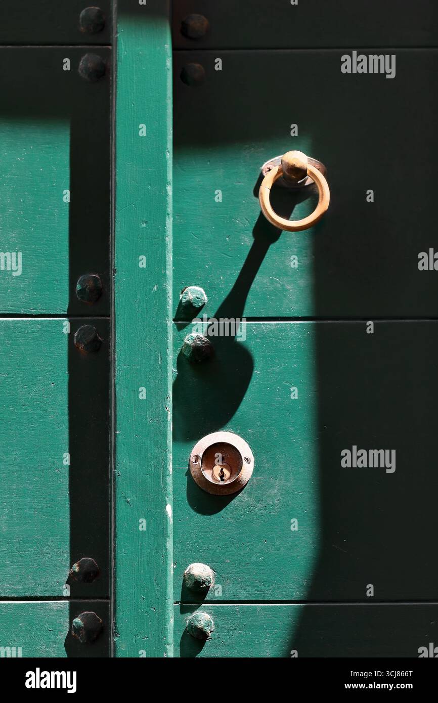 284 bouton de porte en forme d'anneau rouillé et trou de serrure avec plaque d'écusson d'une porte en bois vert cloutée sur la rue via Giovanni Capellini. Porto Venere-Ligurie. Banque D'Images