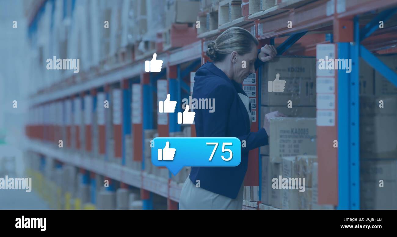 Femme penchée dans le blazer marine inspectant la boîte dans l'allée de l'entrepôt, avec pouce flottant vers le haut, espace de copie Banque D'Images