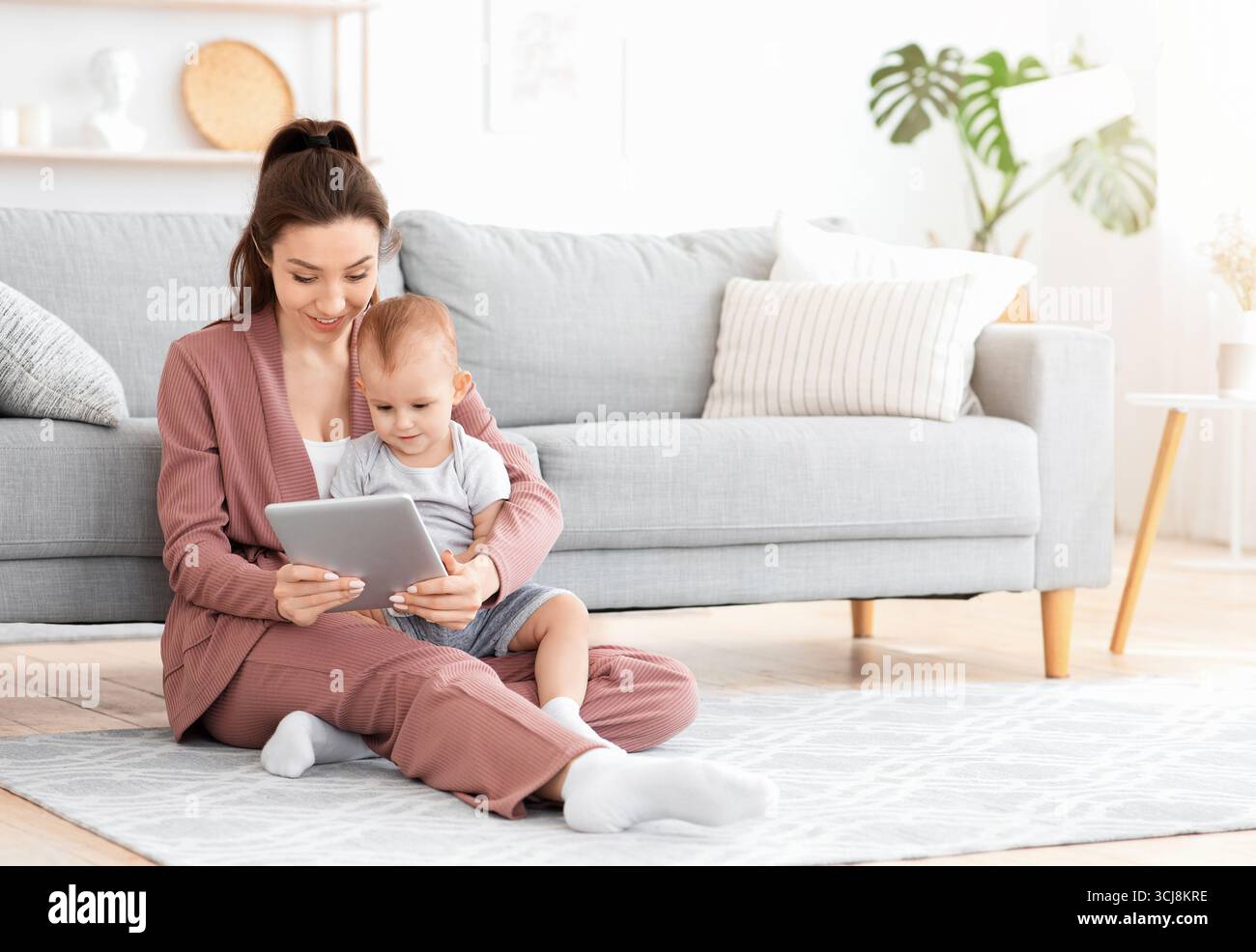 Une mère souriante et son adorable bébé regardent ensemble des caricatures sur une tablette numérique Banque D'Images