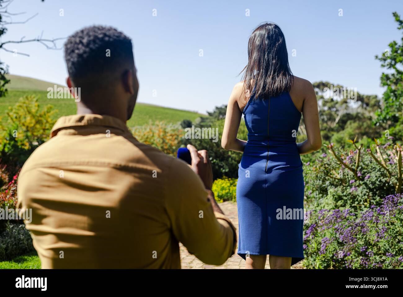 Homme prenant photo de femme en robe bleue à l'extérieur dans le cadre du jardin Banque D'Images