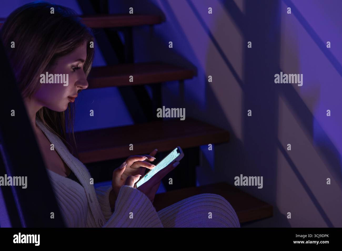 La jeune femme lit des messages au téléphone sous l'ombre des escaliers. Soirée tranquille. Banque D'Images