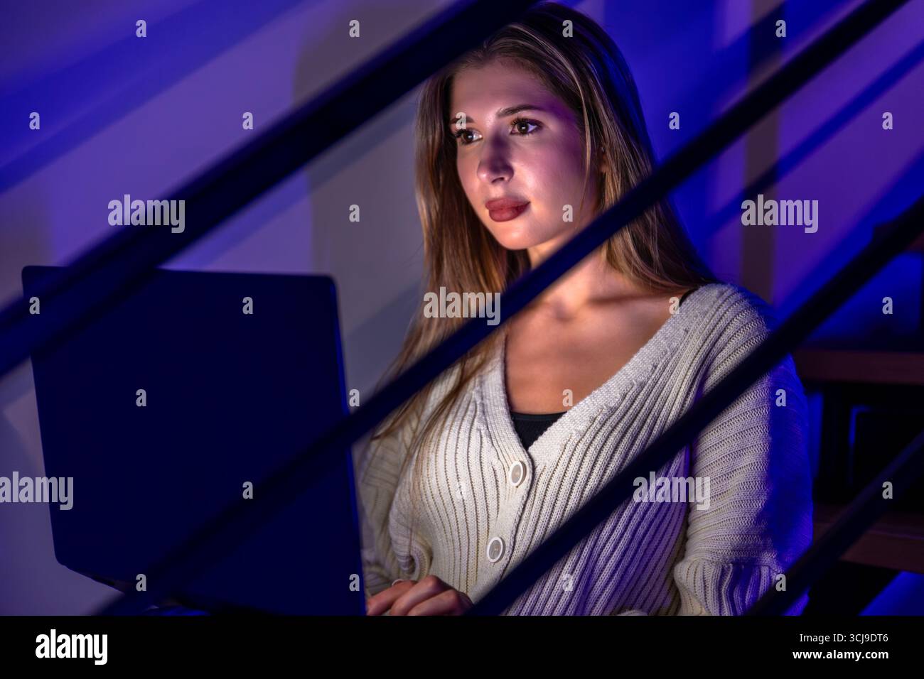 Jeune femme regardant l'ordinateur portable sous la lumière violette bleue. Gros plan. Banque D'Images