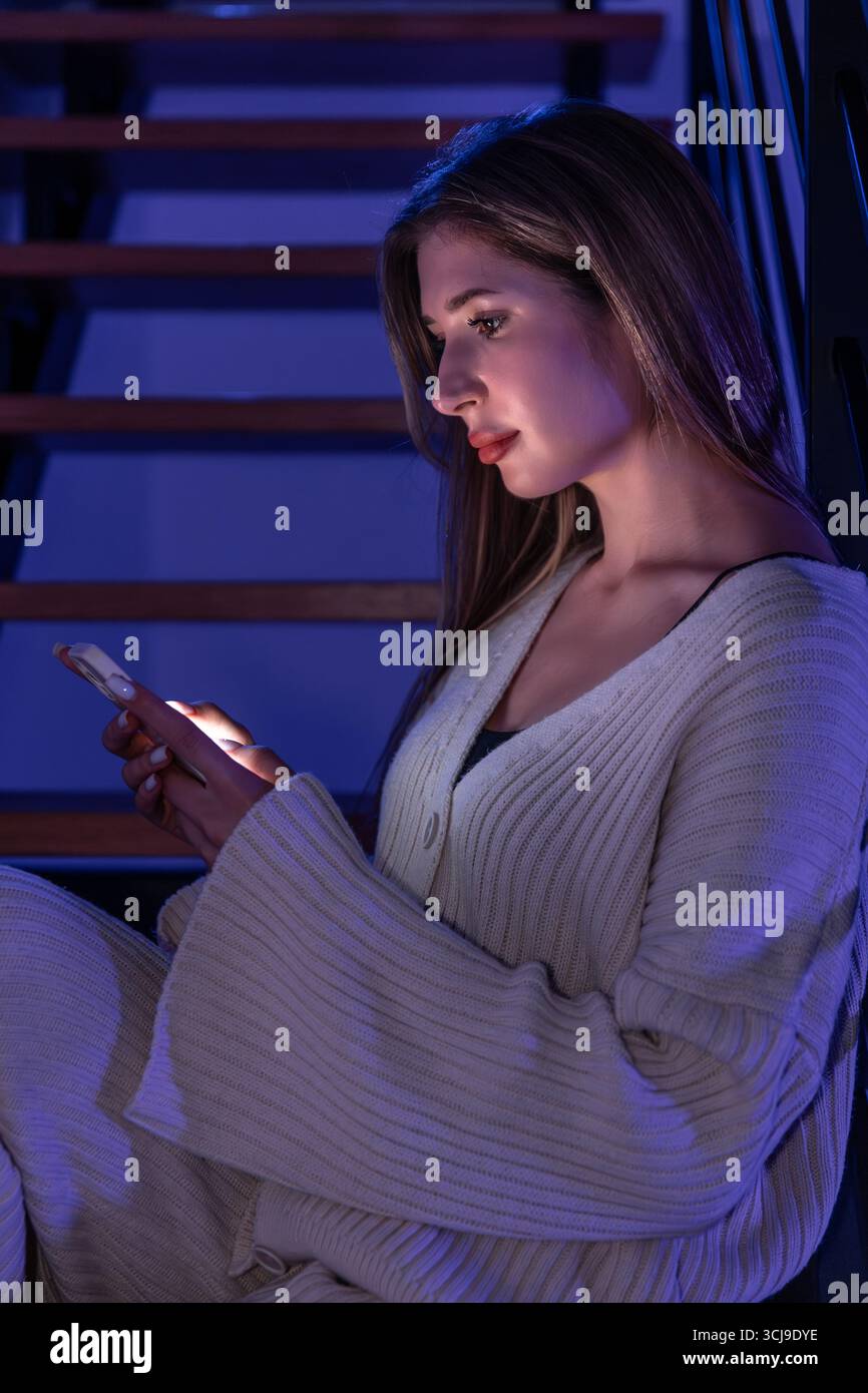 Jeune femme avec smartphone dans les escaliers en néon bleu. Défilement nuit. Banque D'Images