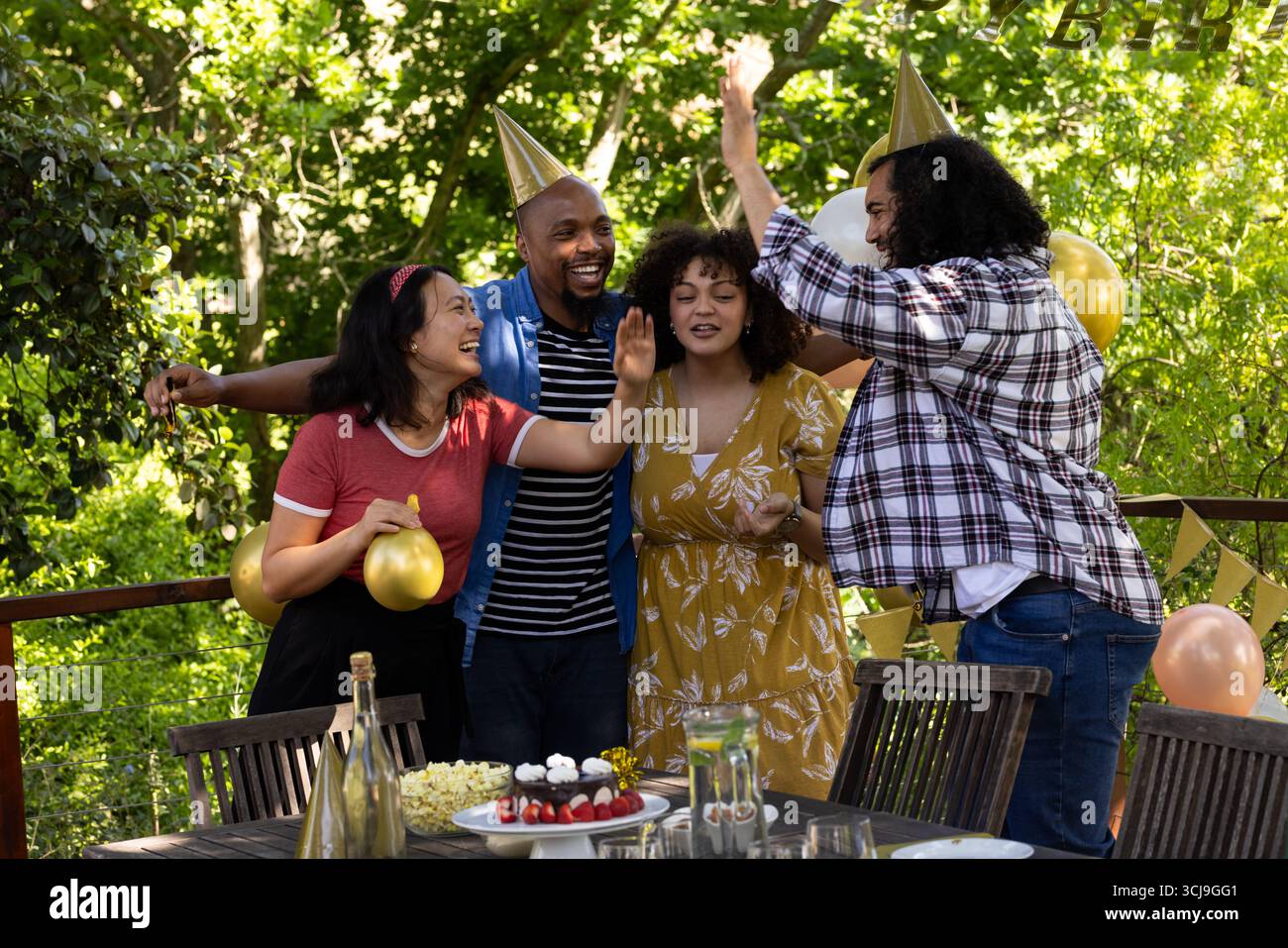 Célébrant en plein air, des amis portant des chapeaux de fête avec des ballons lors d'une réunion festive Banque D'Images